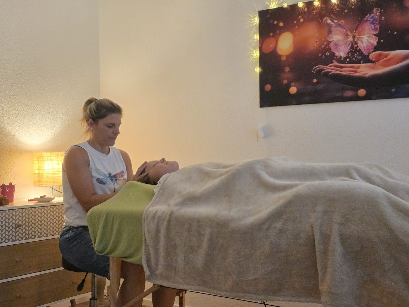 Therapeutin bei der Hypnose-Arbeit am liegenden Klienten, warmes Licht, Butterfly-Kunstwerk an der Wand